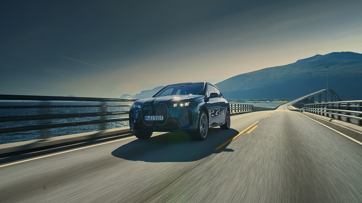 3/4 Frontansicht eines auf einer Brücke entlang einer Küste fahrenden BMW iX